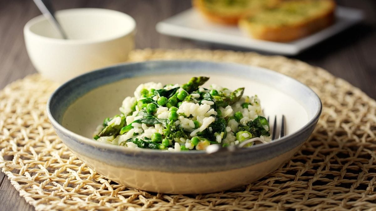 Veganes Spargelrisotto mit Spinat und Erbsen auf einem tiefen Teller mit einer Gabel.