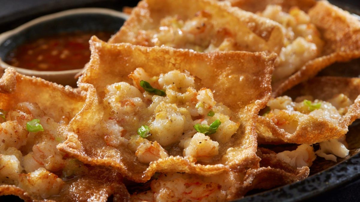 Wan Tan Blätter mit Garnelenmasse in der Pfanne ausgebacken, auf einem schwarzen Teller mit Sweet-Chili-Sauce.