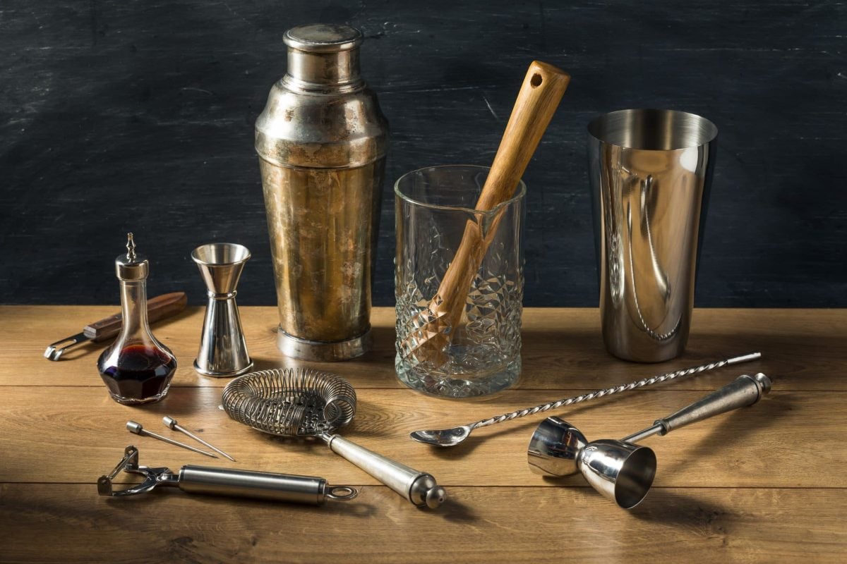 Zum Cocktail-Tag in den USA Barwerkzeuge und Cocktail-Zubehör Basisausstattung auf Holztisch vor schwarzem Hintergrund. Frontalansicht.