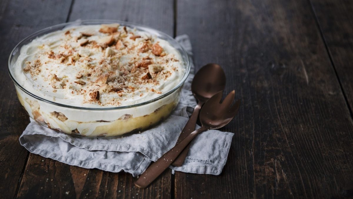 Zitronen-Quark-Trifle mit Keksen in einer durchsichtigen Auflaufform geschichtet und serviert auf einem dunklen Holztisch.