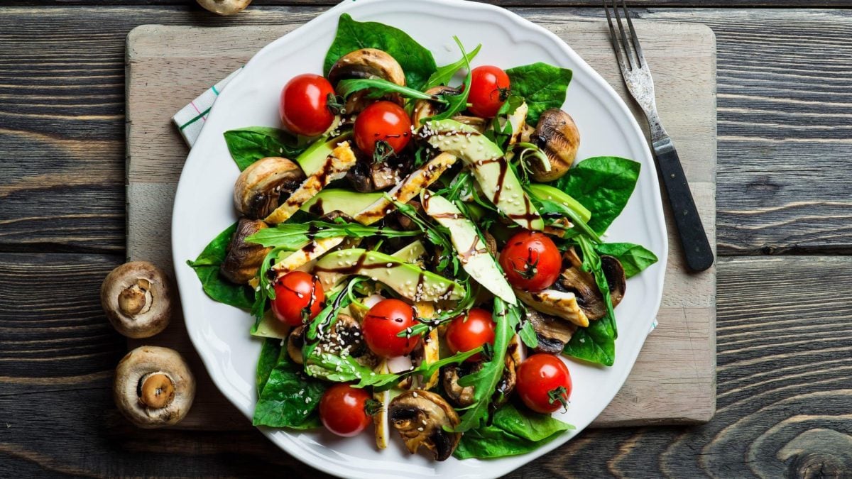 Avocado-Salat mit Pilzen und Tomaten auf weißem Teller, angerichtet auf hölzernem Untergrund