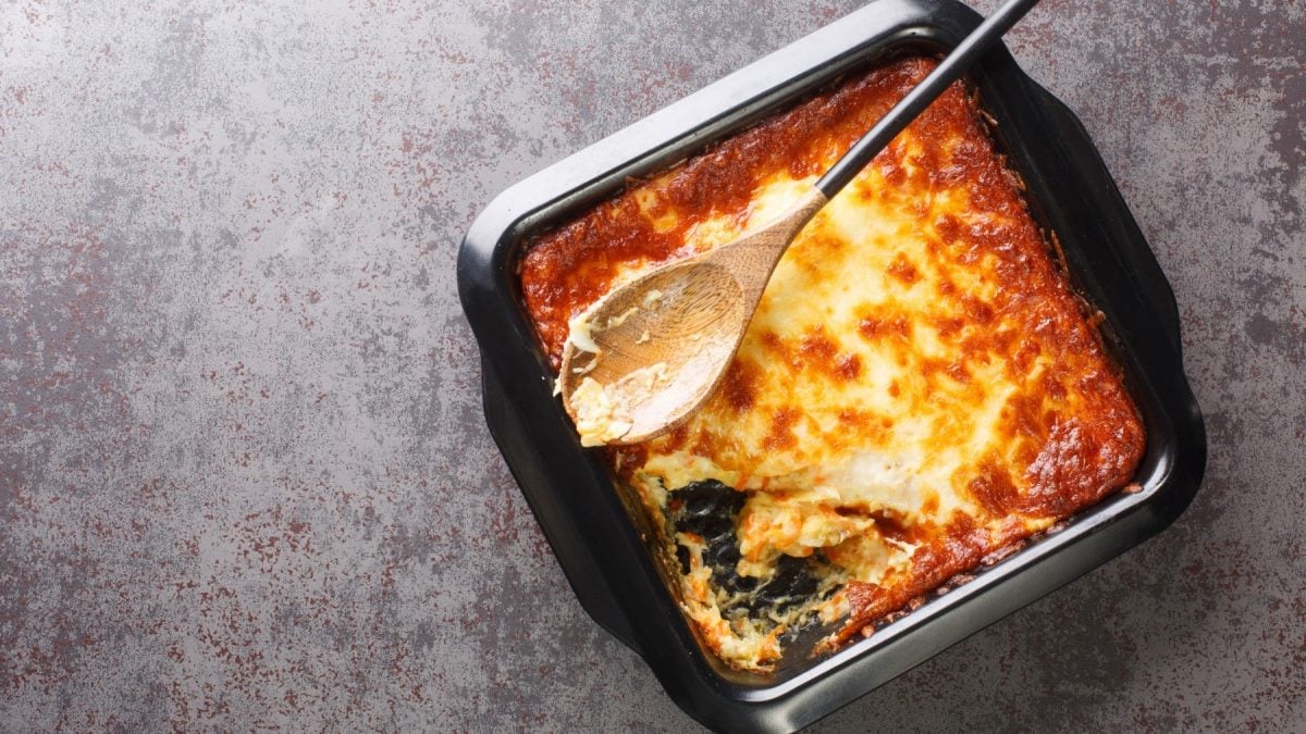 Bacalhau espiritual in einer schwarzen Auflaufform mit einem hölzernen Kochlöffel.