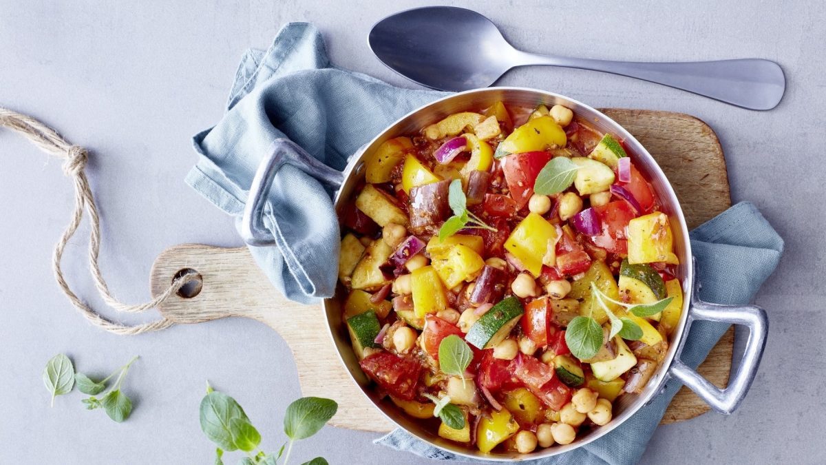 Blitz-Ratatouille mit nussigen Kichererbsen in einem großen Topf, serviert auf einem Holzbrett auf hellem Untergrund.
