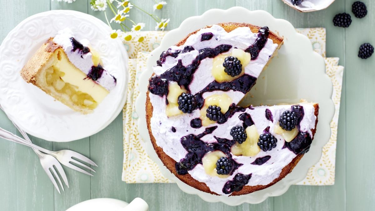 Auf einem Teller steht eine Birnen-Brombeer-Schmandtorte. Sie ist mit Brombeeren und Birnen und einer Creme bedeckt.