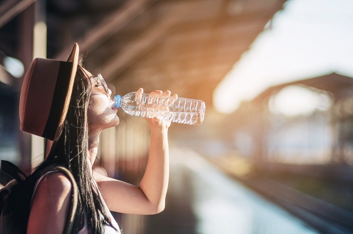 Frau trinkt Wasser aus Flasche an einem sonnigen Bahnhof