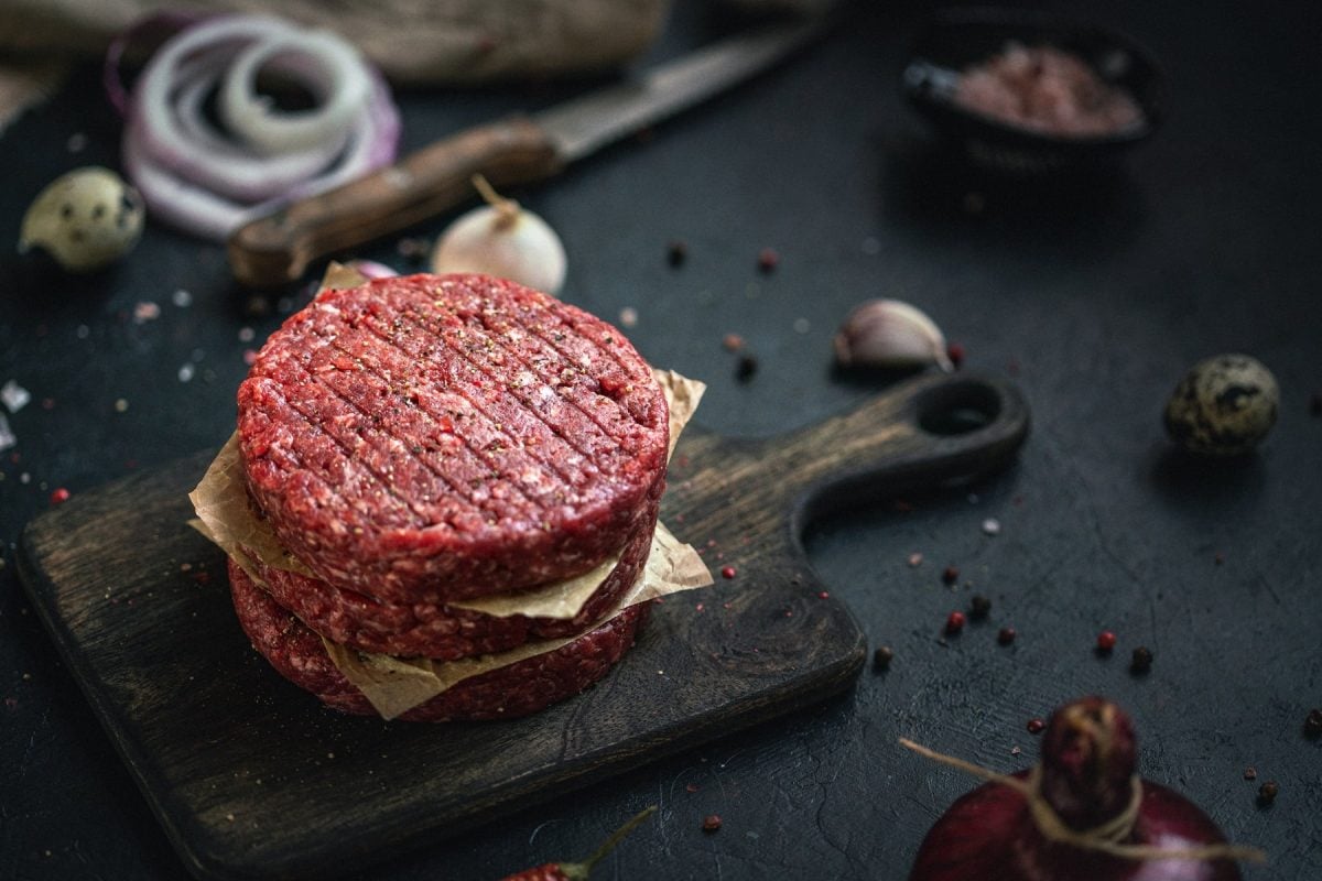 Drei Hackfleisch-Pattys auf dunklem Holzbrett.