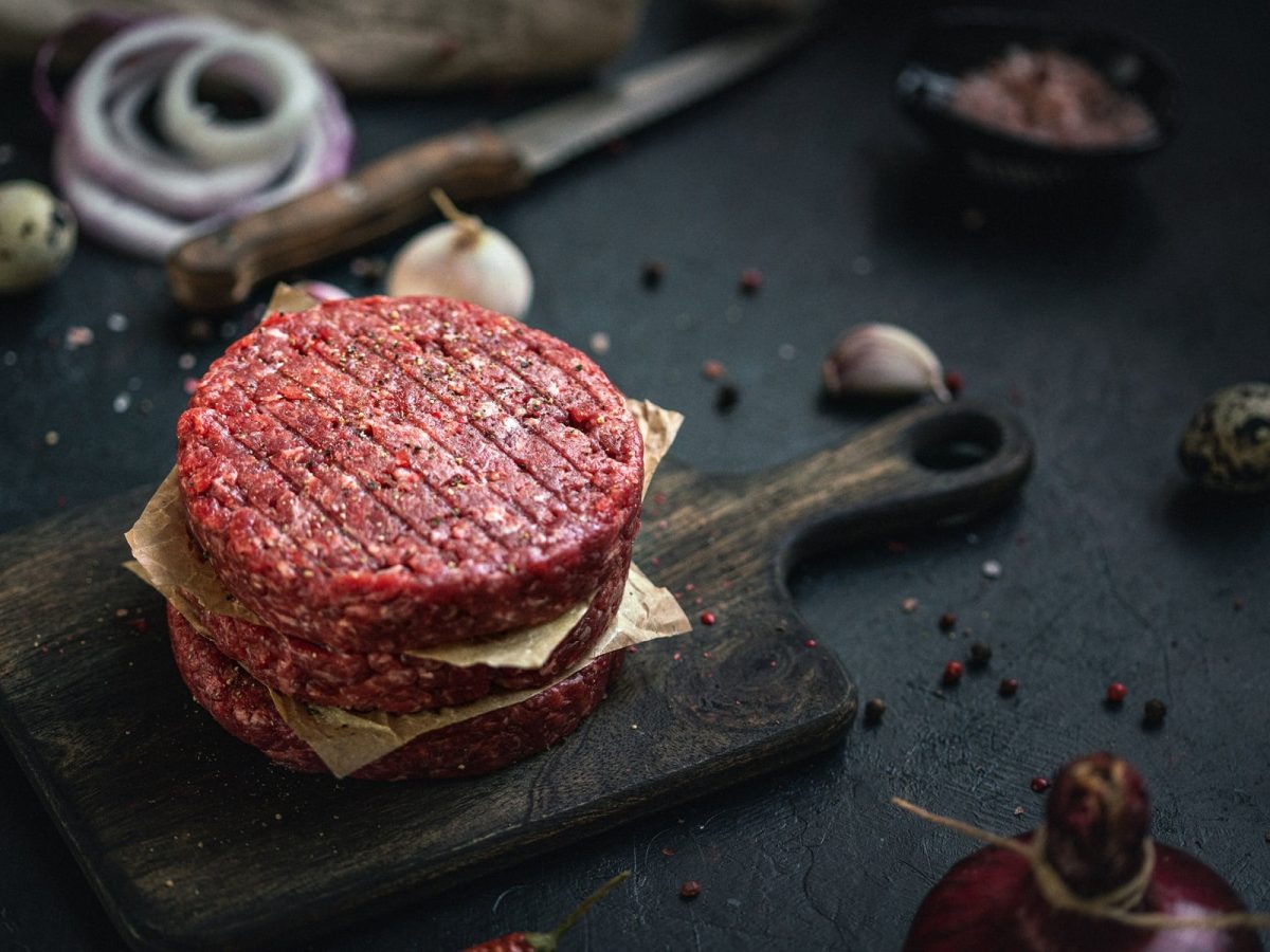 Drei Hackfleisch-Pattys auf dunklem Holzbrett.
