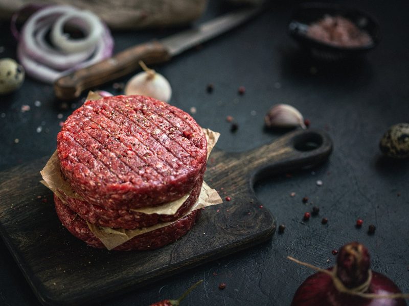 Drei Hackfleisch-Pattys auf dunklem Holzbrett.