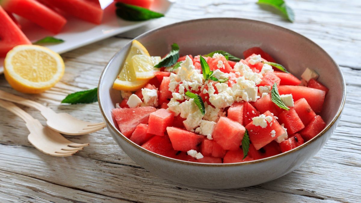 Eine Schale mit Wassermelone, Feta und Minze auf hölzernem Untergrund.