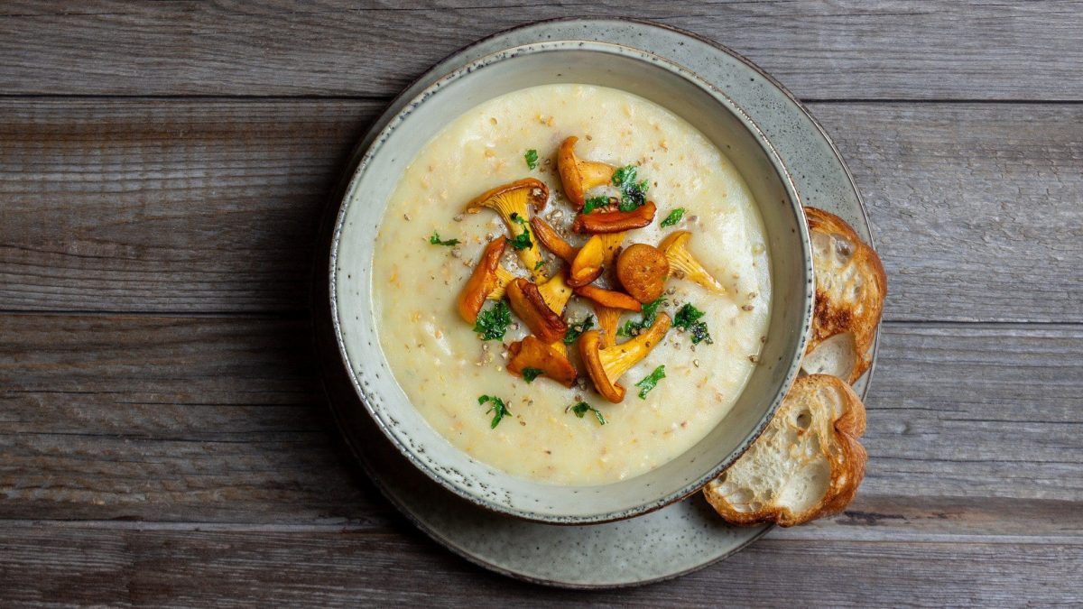 Pfifferling-Cremesuppe mit gebratenen Pfifferlingen auf hölzernem Untergrund.