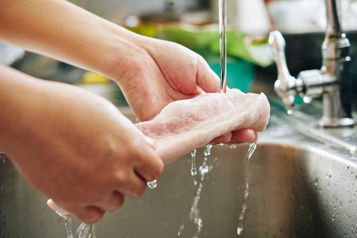 Rohes Fleisch wird unter Wasserhahn abgewaschen.