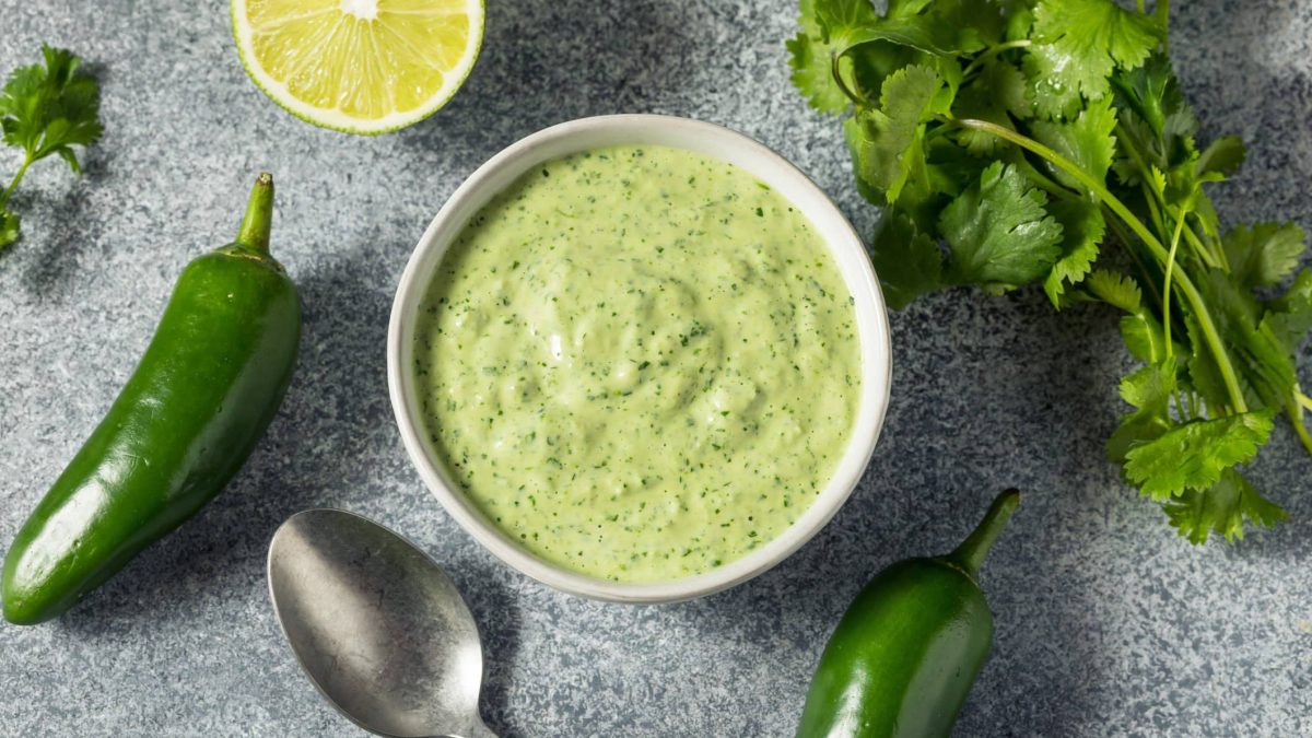 Grüne Aji-Sauce aus Peru in einem Gefäß neben grüner Chili, Limette und Koriander