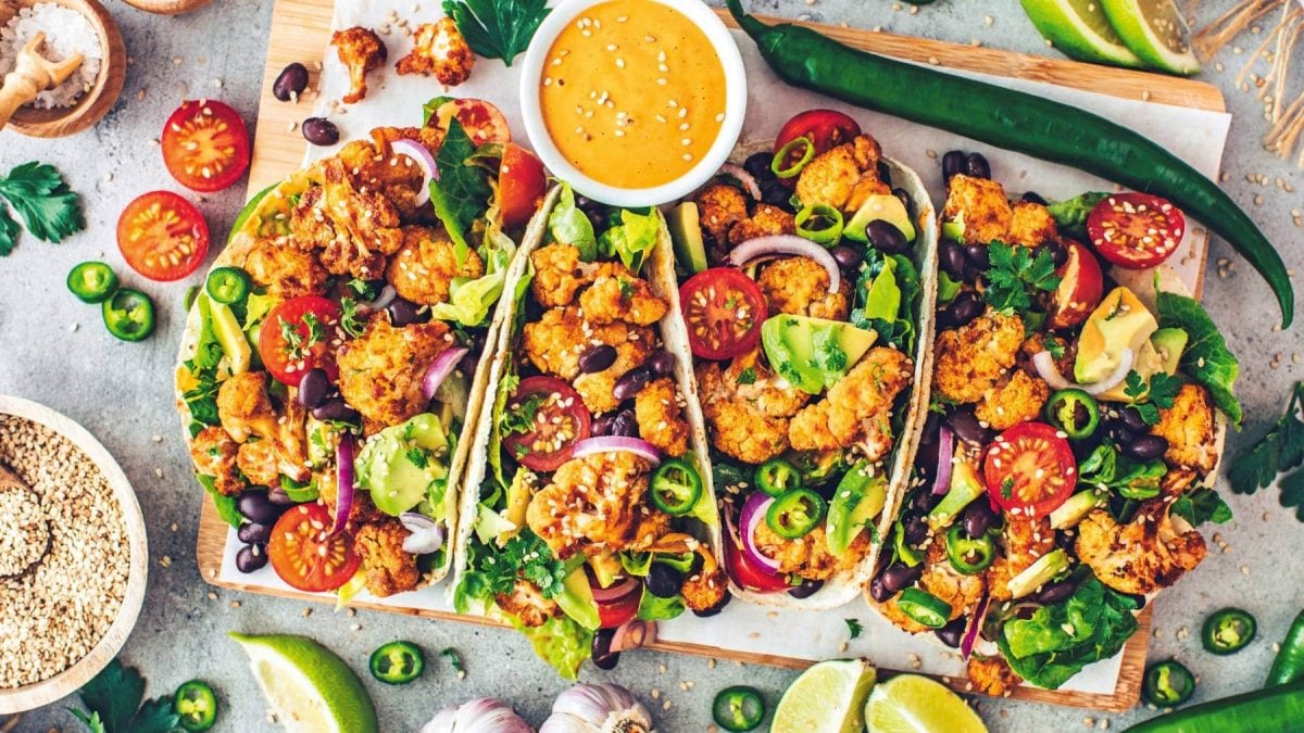 Blumenkohl-Tacos mit Avocado, Tomaten und weiterem Gemüse in der Draufsicht, daneben lieben Zutaten verstreut.