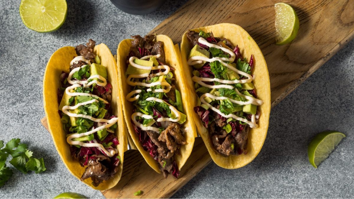 Bulgogi Tacos auf einem braunen Brett neben frischen Limetten und Koriander