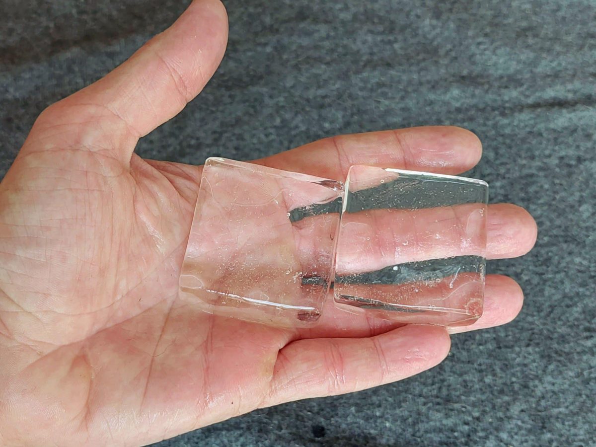 Eine Hand mit zwei durchsichtigen Eiswürfeln auf grauem Untergrund.
