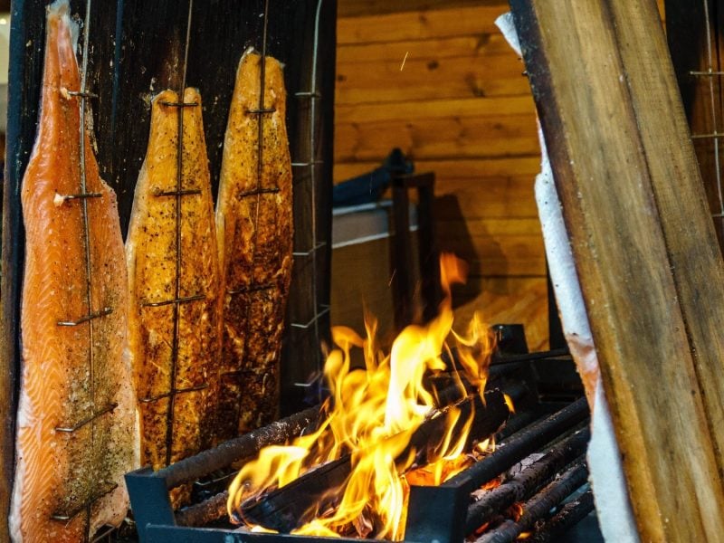 Fünf Bretter mit Flammlachs am offenen Feuer stehend.