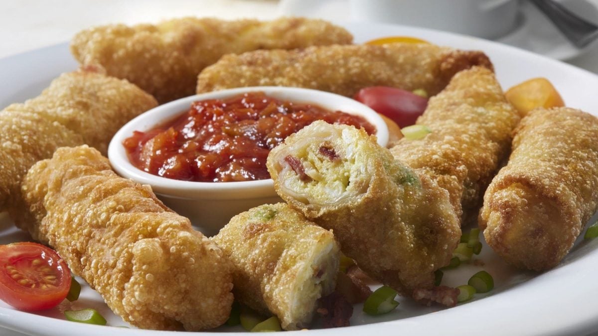 Frittierte Frühstücks-Frühlingsrollen, gefüllt mit Rührei mit Speck und Frühlingszwiebeln, serviert mit einer Salsa und frischen Cherry-Tomaten.