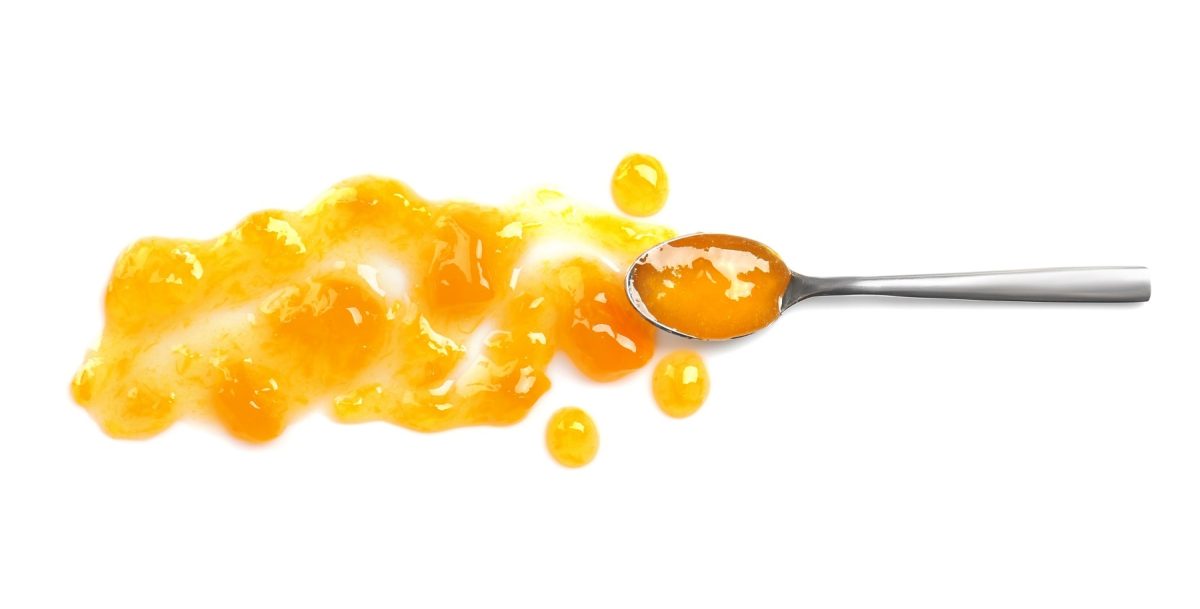 ein Loeffel mit einer orangen Fluessigleit liegt auf einem weißen Untrgrund