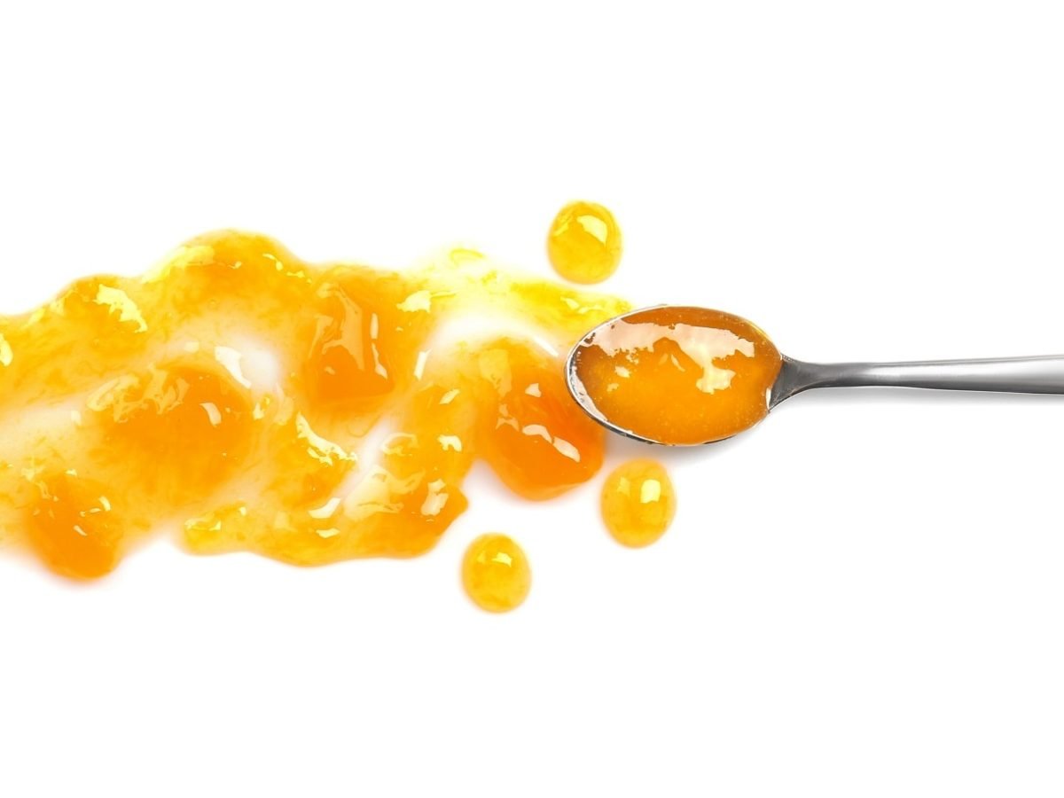 ein Loeffel mit einer orangen Fluessigleit liegt auf einem weißen Untrgrund