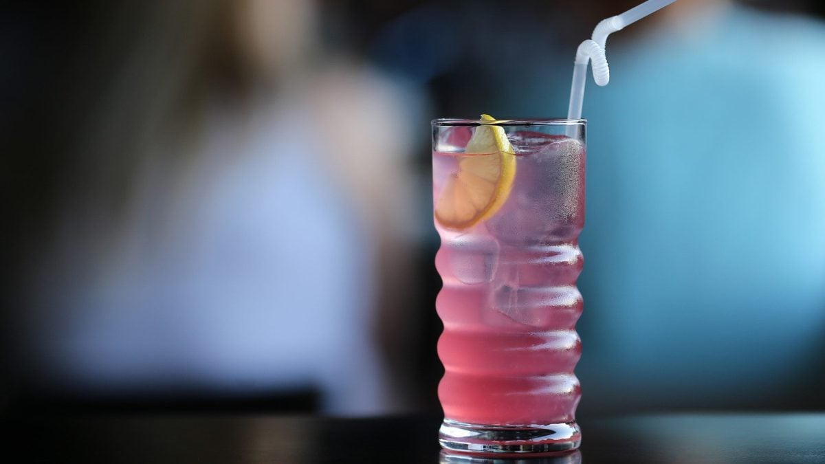 Gin Rosé Gin Cocktail mit Rosé Wein in besonderem Longdrink-Glas auf schwarzem Untergrund vor Bargästen.
