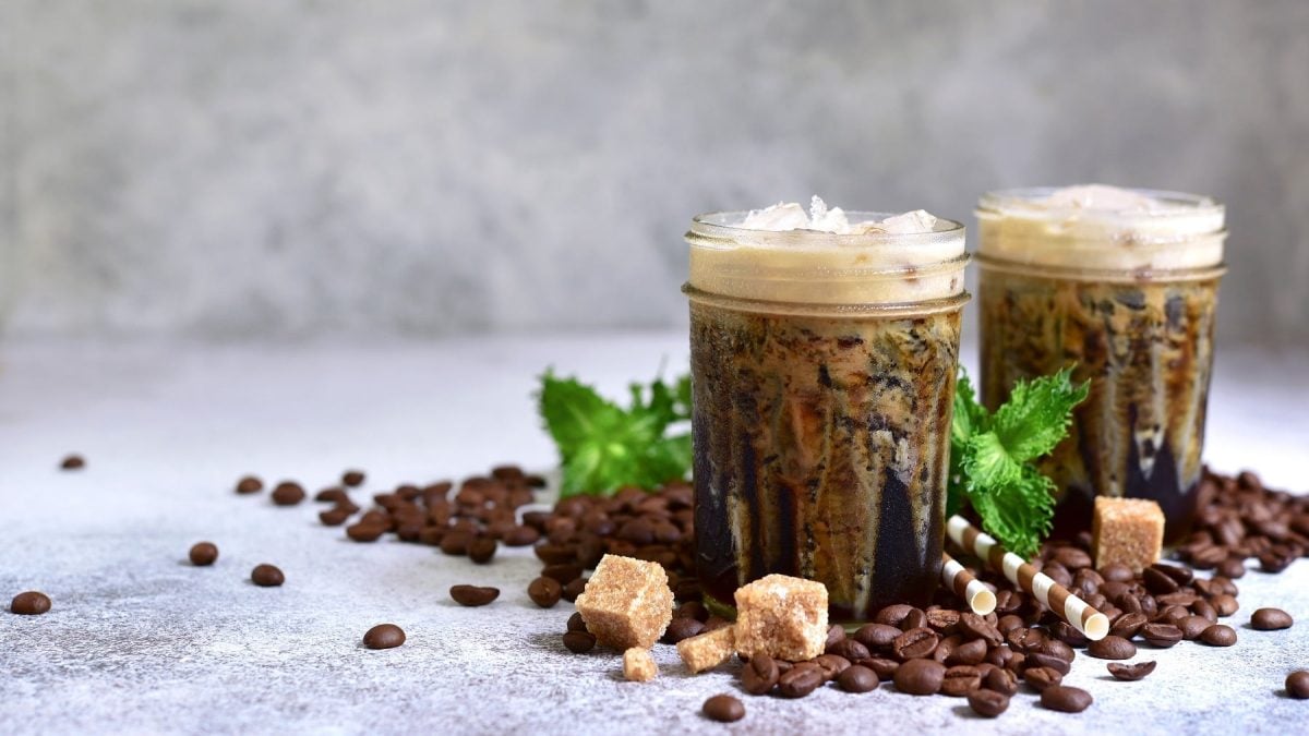 Zwei Gläser griechischer Frappé, drumherum Kaffeebohnen, Zuckerwürfel und Strohhalme.