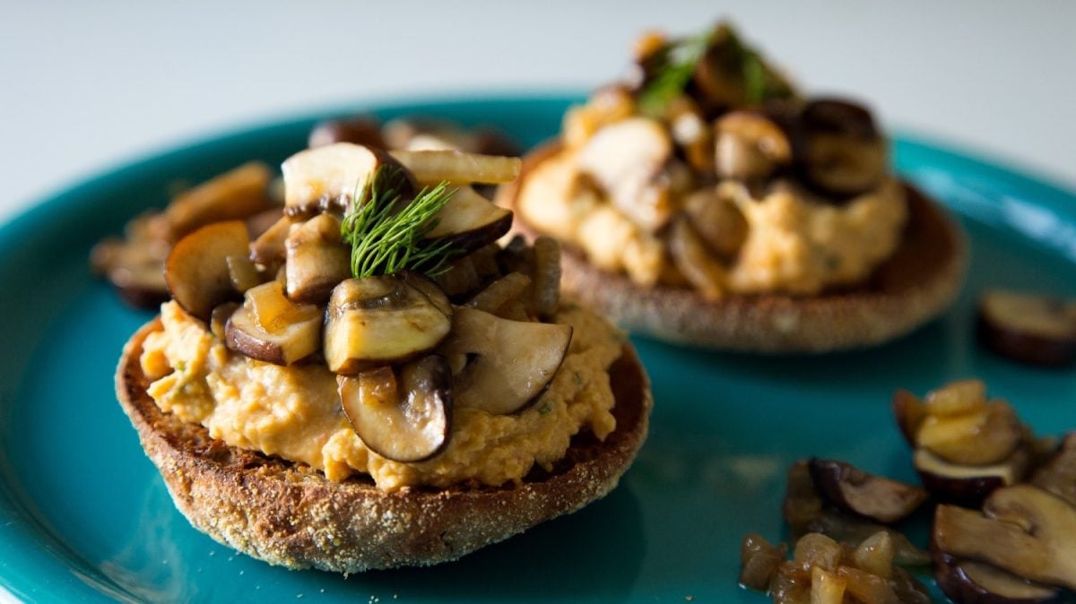 Drei Toasties auf einem blauen Teller mit Hummus und gebratenen Pilzen garniert.
