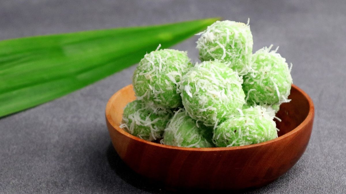 Eine braune Schale mit einigen der grünen Klebreisbällchen. Im Hintergrund ist ein Pandan-Blatt zu sehen.