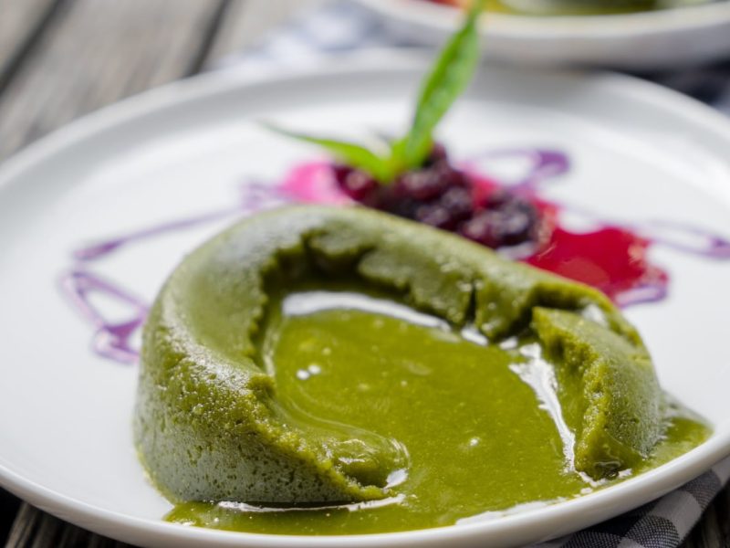 Ein zerlaufender Matcha Lava Cake auf einem weißen Telle r mit etwas Beerenragout.