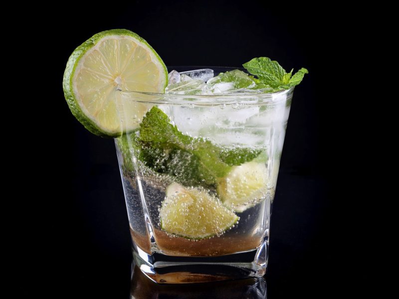 Ein Glas Mojito vor einem komplett schwarzen Hintergrund.
