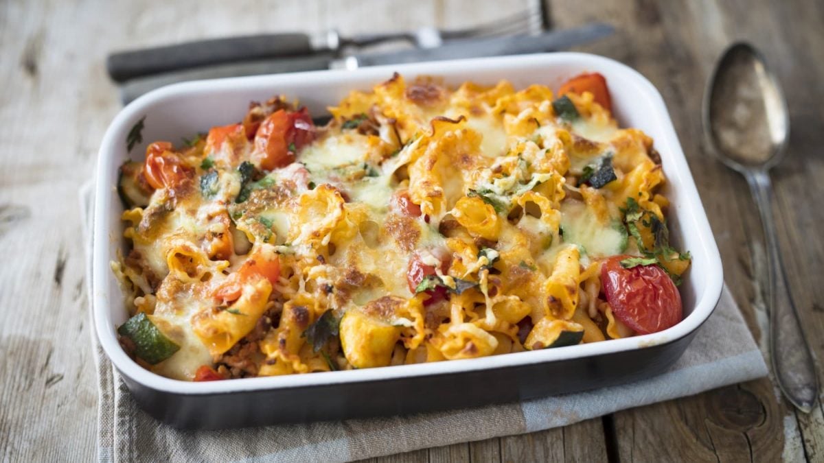 Nudelauflauf mit Zucchini und Paprika in einer Auflaufform. Diese steht auf einem Küchentuch und daneben liegt Besteck.
