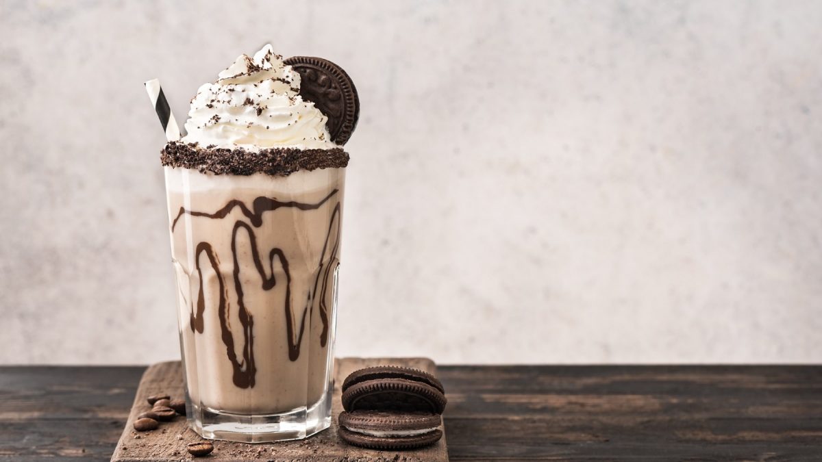 Ein Glas Schokokeks-Milchshake mit Strohhalm, Sahnehaube und Keks, daneben liegen zwei Kekse.