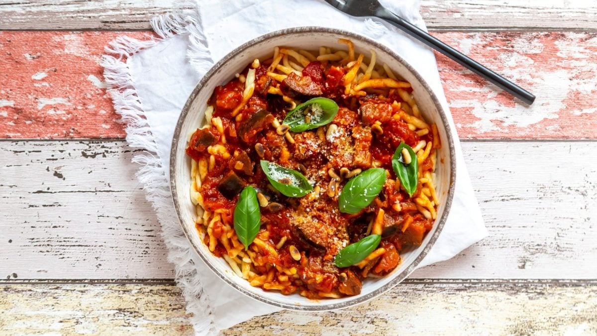 Ein Teller Pasta mit veganer Frischkäsesauce und frischem Basilikum in der Draufsicht, daneben eine Gabel.