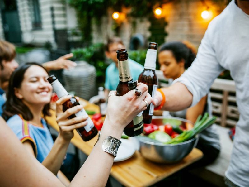 Pfingst-Grillen im Wildwuchs Brauwerk: eine Gruppe junger Menschen sitzt draußen an einem Tisch und stößt mit Bier an.