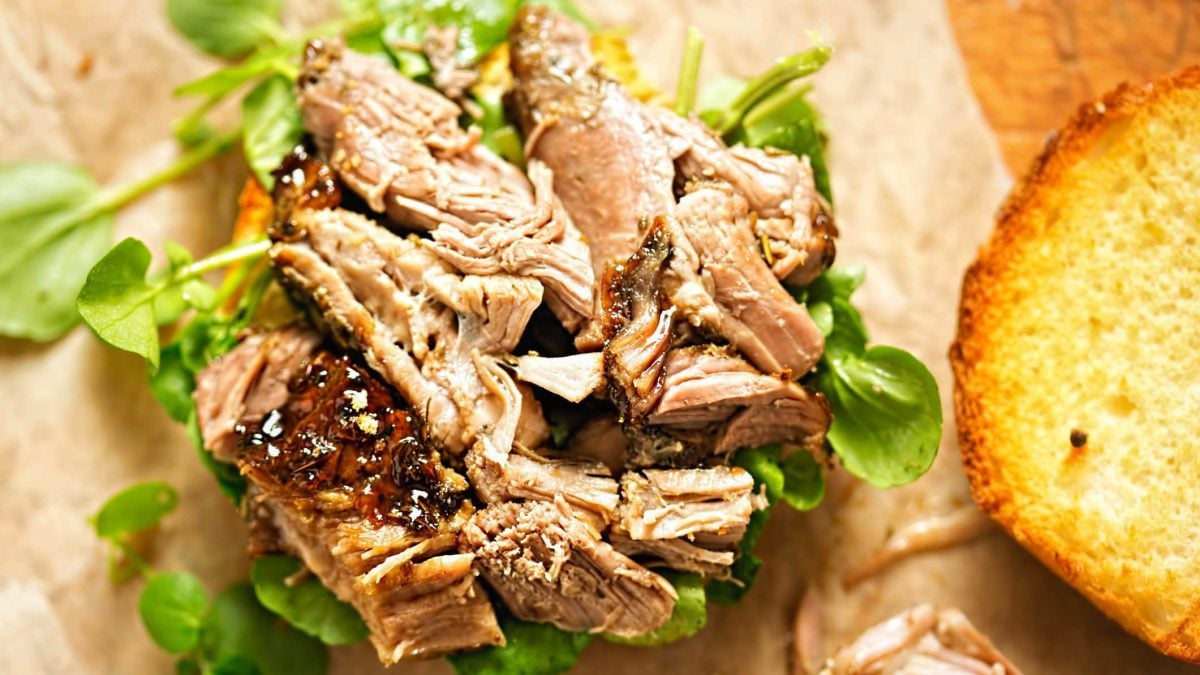 Tükisches Pulled Lamb Denizli Kebap auf Salatbett und hellem Untergrund. Daneben geröstetes Brot. Aufnahme aus der Vogelperspektive.