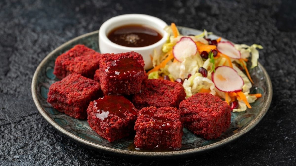 Rote-Bete-Tofu-Würfel auf einem grauen Teller mit Granatapfelsauce und etwas gemischtem Salat. Alles auf einem dunklen Untergrund.