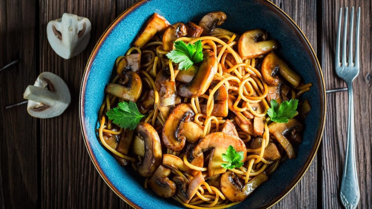 Spaghetti mit Sojabutter und Pilzen in einer blauen Schüssel auf einem Holztisch