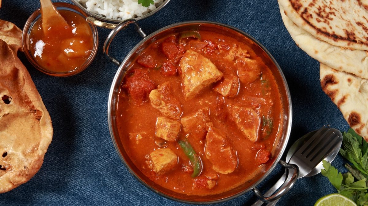 Eine Schale Tandoori Masala auf dunkelblauem Untergrund mit Naan an der Seite.