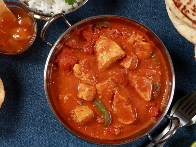 Eine Schale Tandoori Masala auf dunkelblauem Untergrund mit Naan an der Seite.