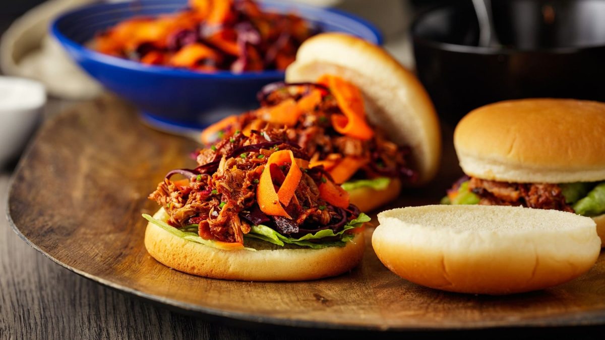 Drei vegane Jackfruit-Burger mit Coleslaw auf einem runden Brett.