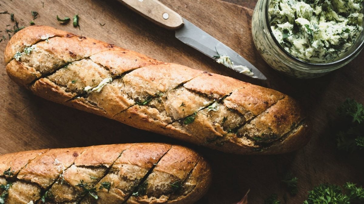 zwei vegane Kräuterbaguettes in der Draufsicht, daneben ein Messer und ein Glas Kräuterbutter.