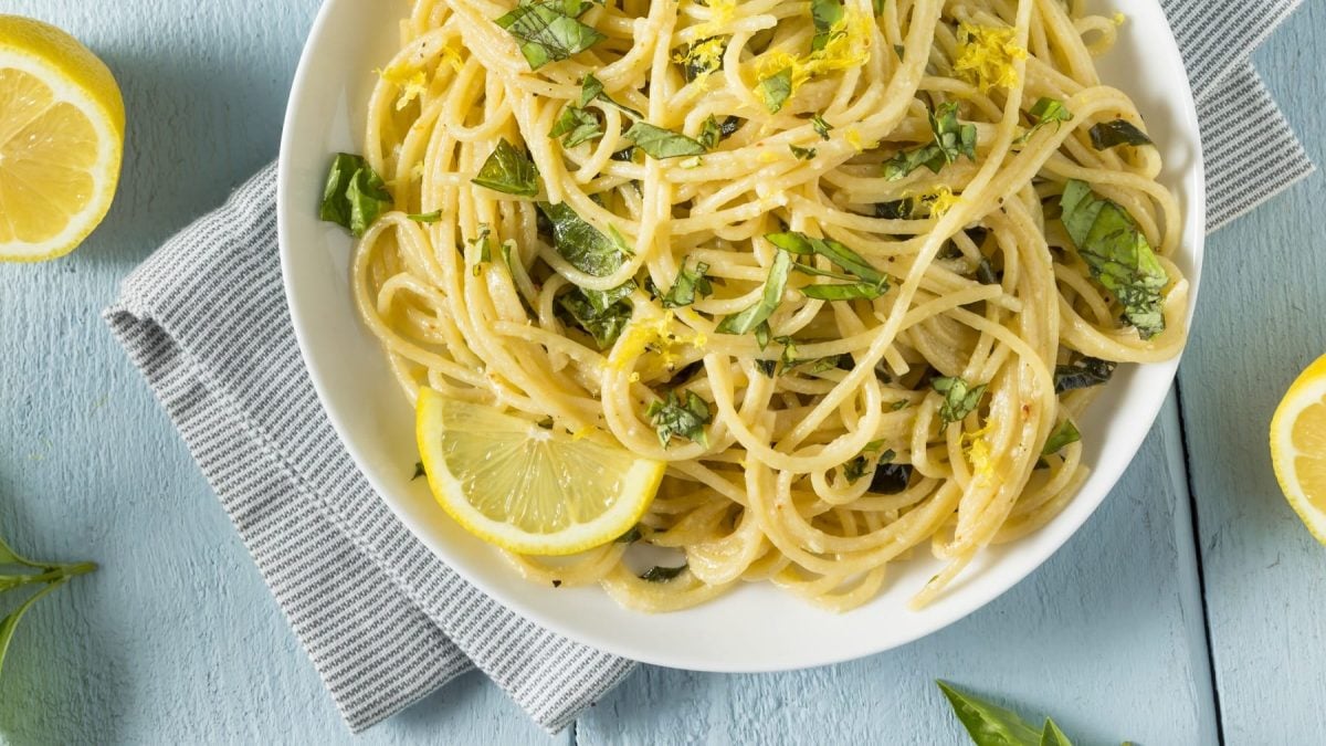 Ein Teller vegane Zitronen-Knoblauch-Pasta mit Zitronenscheiben und gehacktem Basilikum in der Draufsicht.