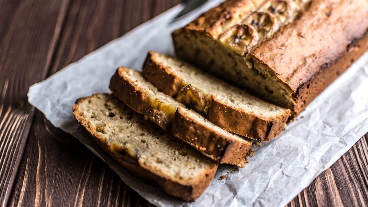 Ein angeschnittenes veganes Bananenbrot mit Bananenscheiben obendrauf.