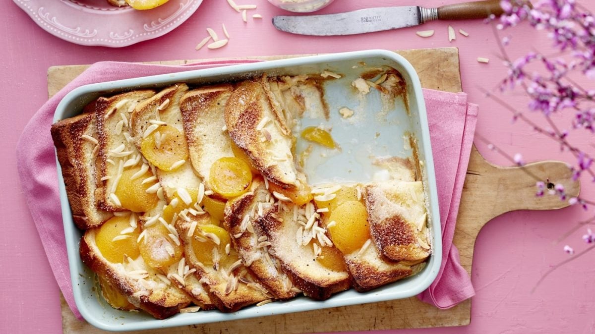 In einer Auflaufform liegt eine Portion Brioche-Aprikosen-Auflauf. Er ist mit Mandelnsplittern und Aprikosen verziert.