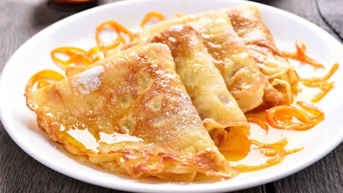 Mehrere Crêpes Suzette mit Orangenzeste auf weißem Teller.