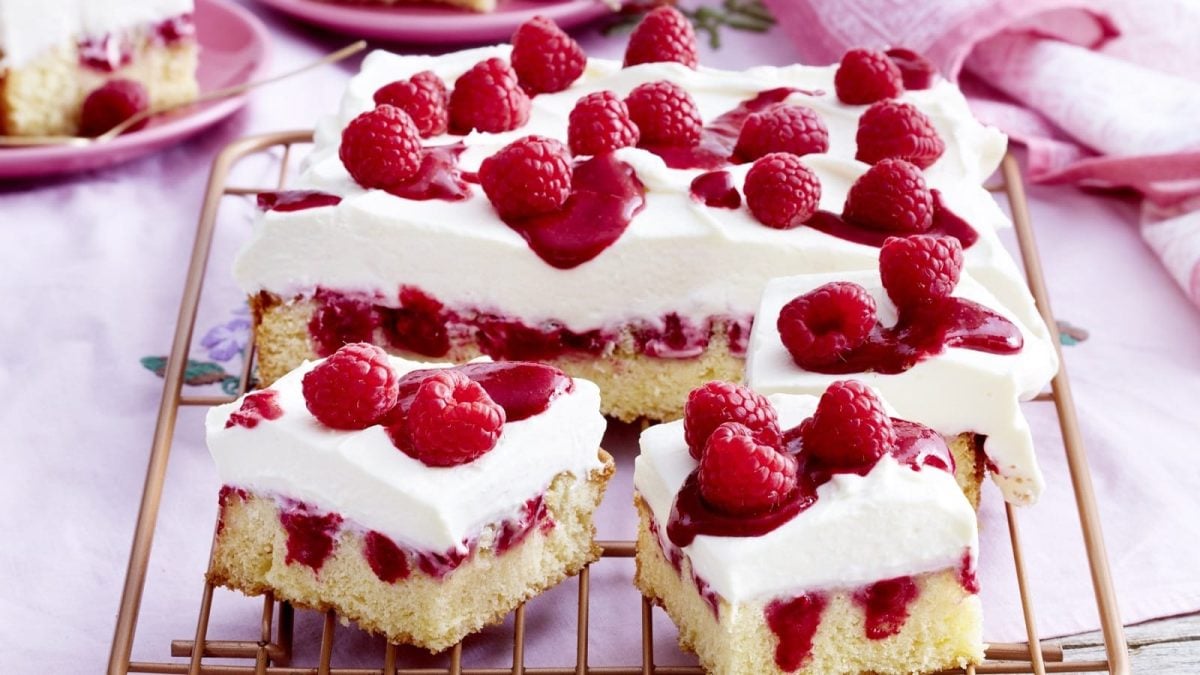 Auf einem Blech liegt ein Himbeer-Mascarpone-Kuchen. Er ist mit einer Creme und Himbeeren verziert.