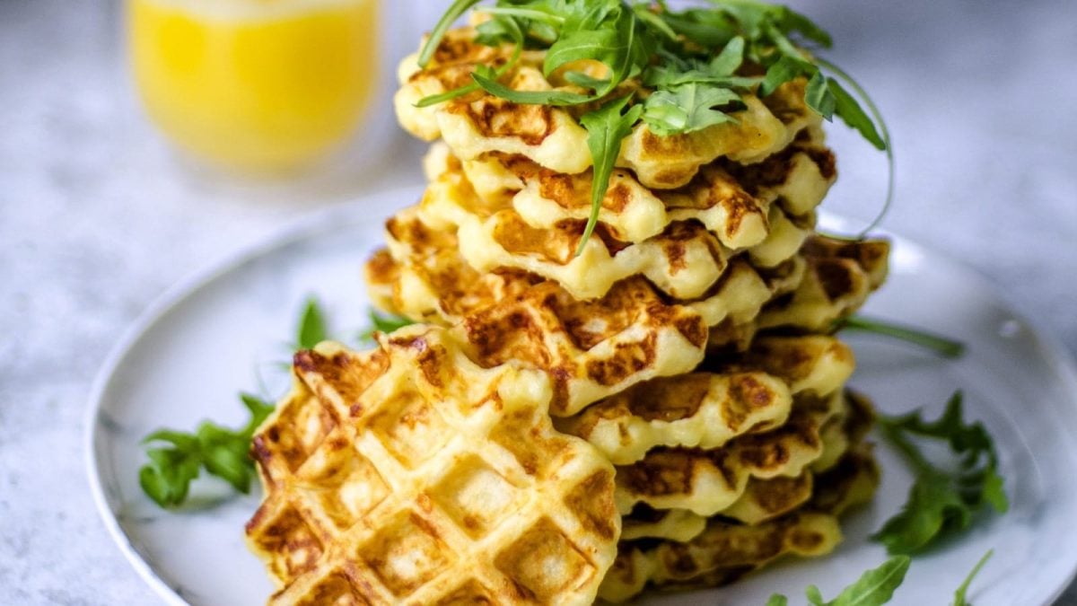 Auf einem Teller liegen mehrere Kartoffelwaffeln mit Rucola und Orangensaft. Sie sind mit Rucola belegt.