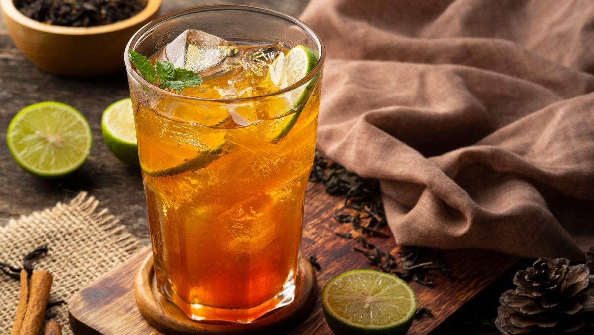Ein Glas mit thailändischem Eistee mit Zitrone neben frischer Limette.
