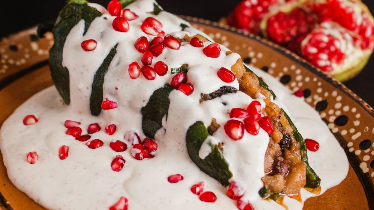 Chiles en nogada gefüllte mexikanische Paprika auf buntem Teller. Daneben Granatapfel. Draufsicht.