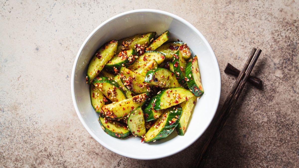 Chinesischer Gurkensalat mit Sesam in einer weißen Schale. Daneben liegen Stäbchen.