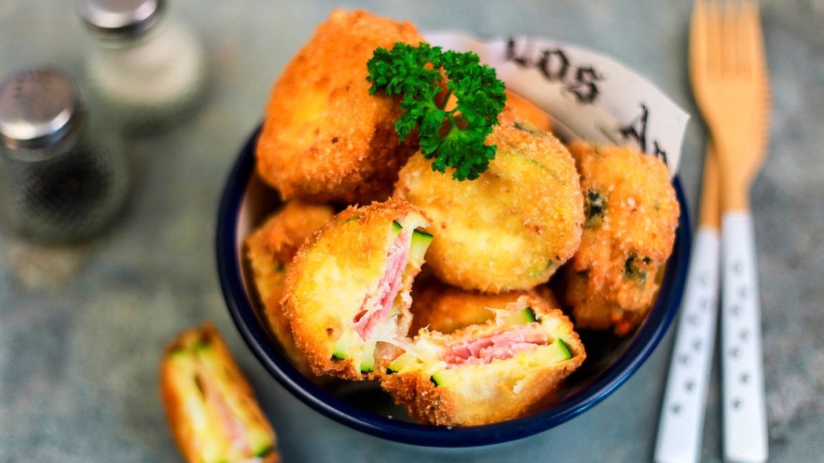 mehrere Cordon Bleu Schnitzel in einer dunklen Schüssel garniert mit Petersilie vor dunklem Hintergrund mit Besteck und Streuern im Hintergrund